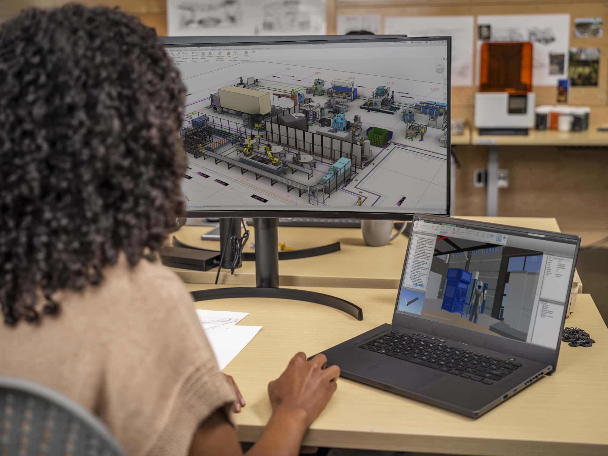 A woman with curly hair looking at a laptop and a computer screen with Autodesk Revit Lt on both. Showing floorplans and building schematics. 